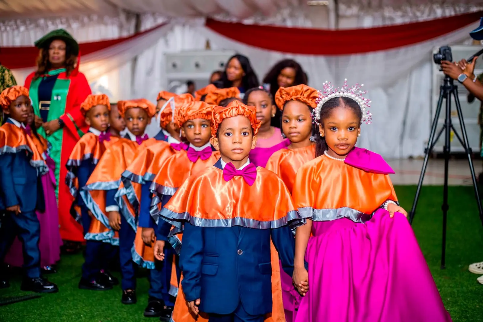 Young graduands in orange capes and caps walking in procession at the 2026 graduation