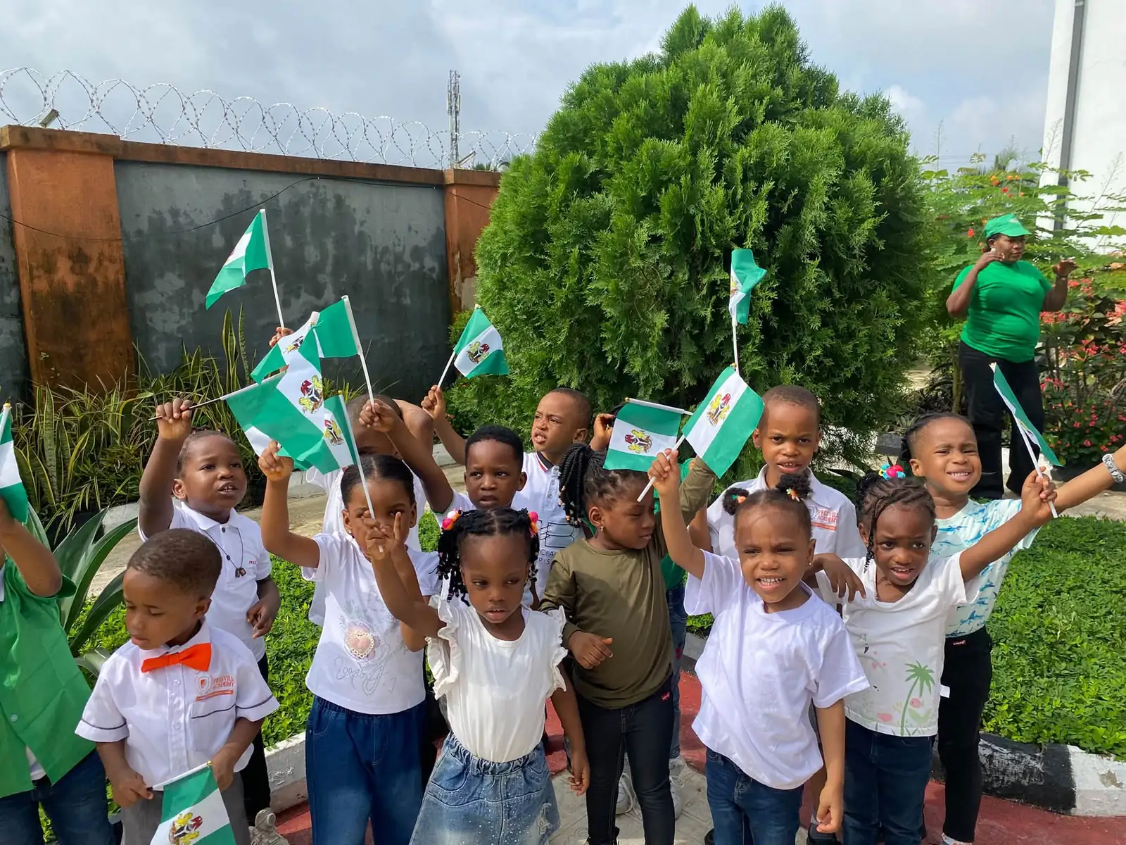 Pupils waving small Nigerian flags outdoors for Independence Day