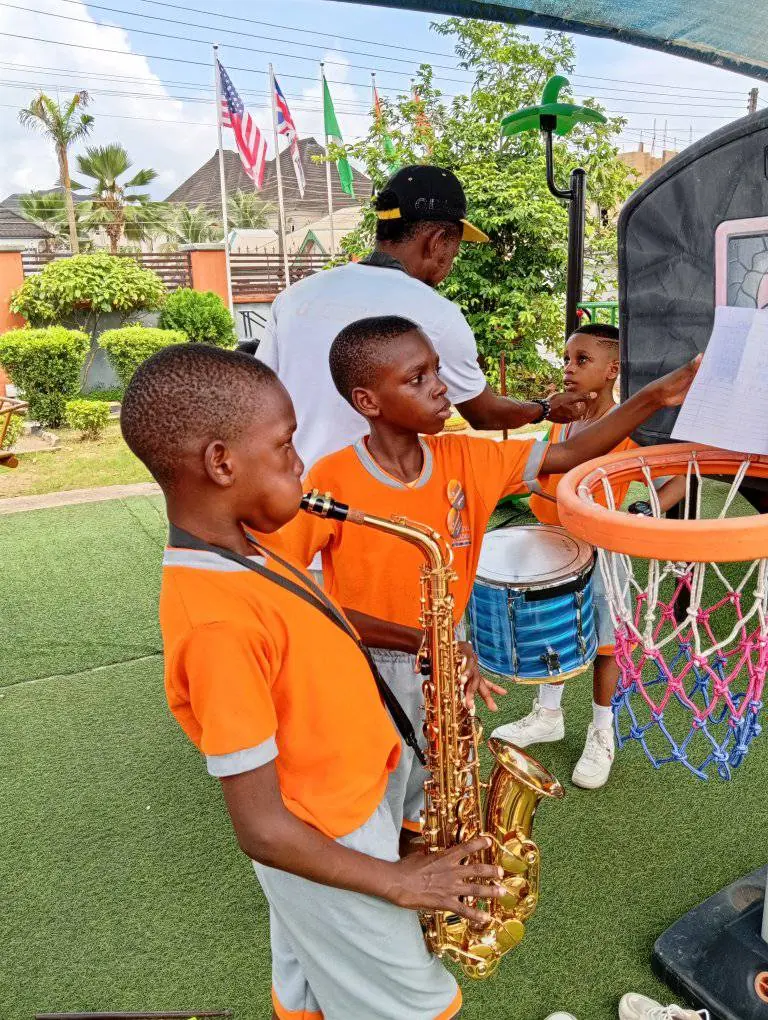 A pupil playing the saxophone outdoors while another plays the drum
