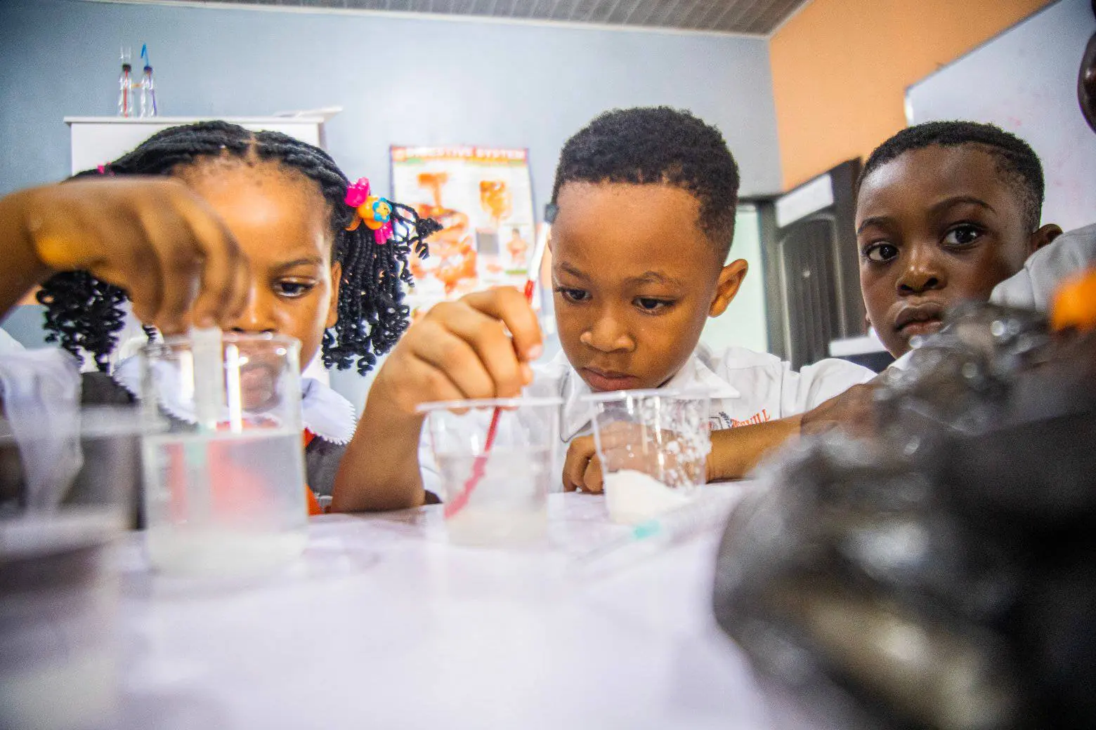 Young pupils measuring powder into beakers during a science lesson