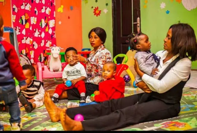 Creche carers playing with babies and toddlers on a soft mat in a brightly painted room