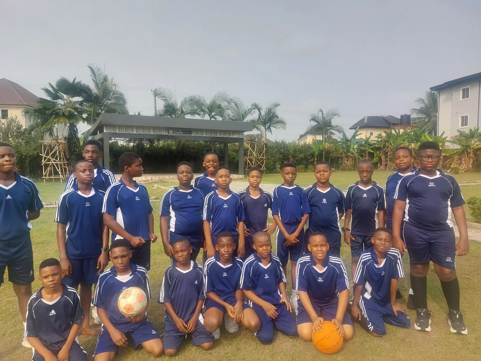 A boys' football team in navy kits posed on a grass pitch with two footballs