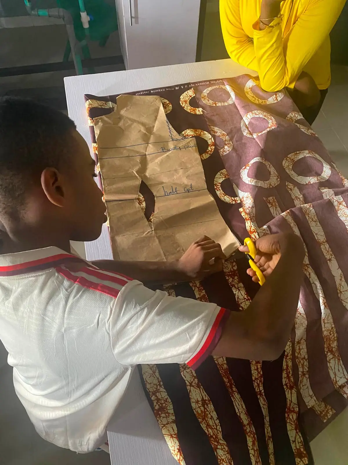 A pupil cutting fabric along a paper pattern during a garment-making lesson