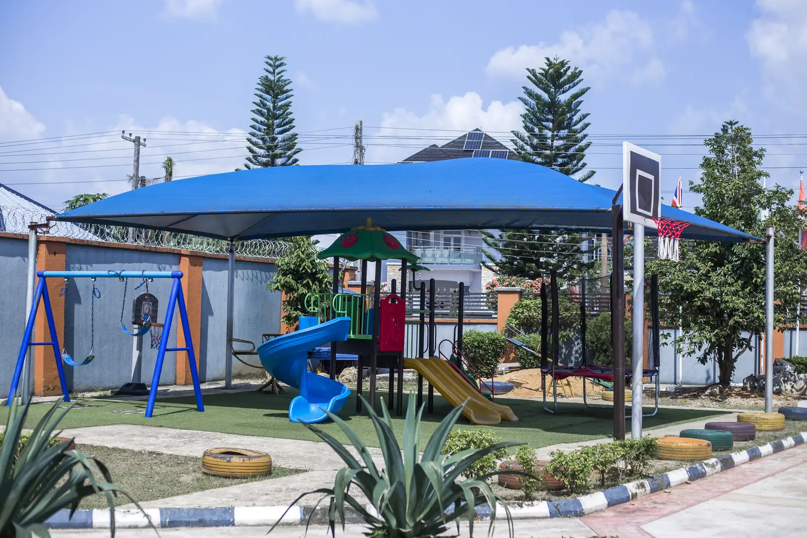 The shaded playground at Presvill Academy, with slides, swings and a basketball hoop on artificial turf