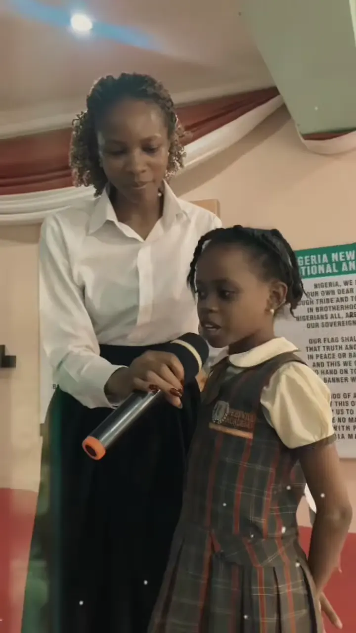 A pupil speaking into a microphone beside a teacher at the Akwa Ibom Day celebration