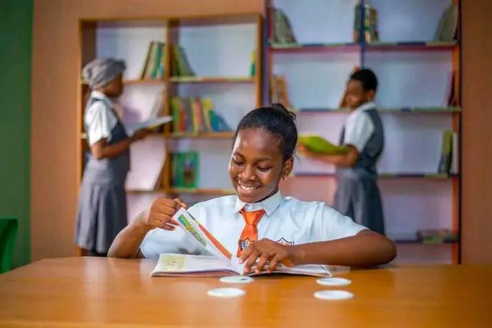 A student reading at a table in the library, with full bookshelves behind her