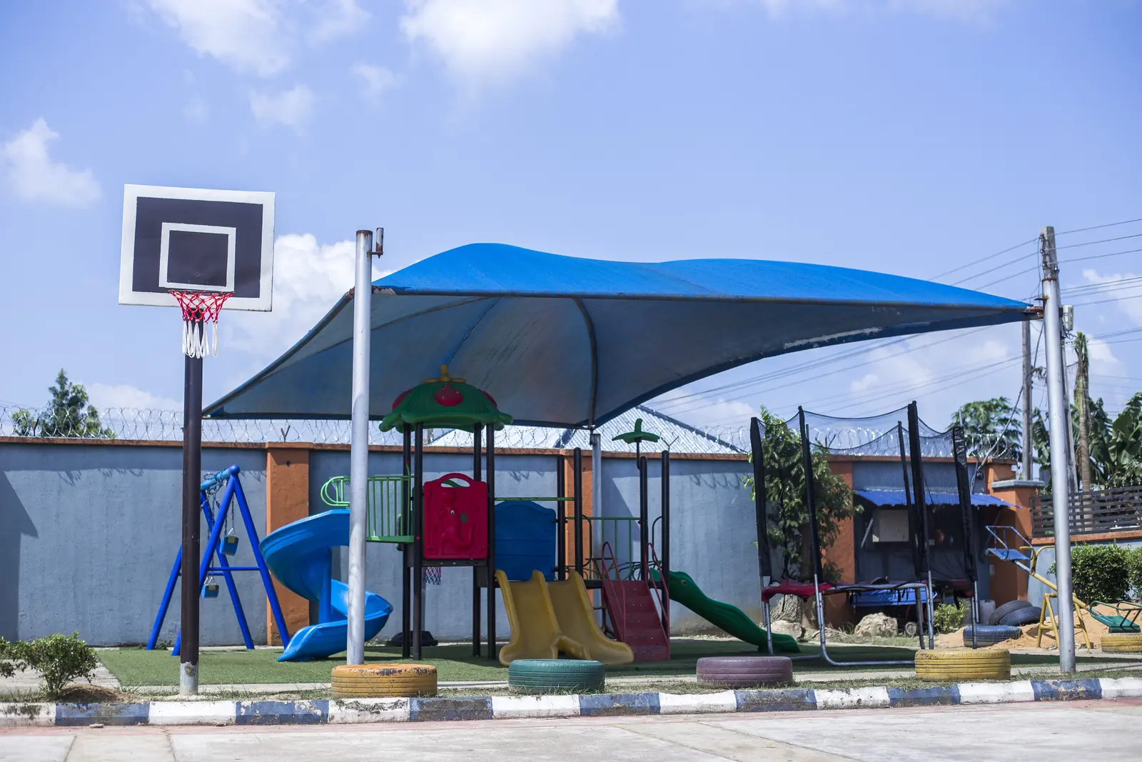 The playground, with slides and climbing frames under a large blue shade