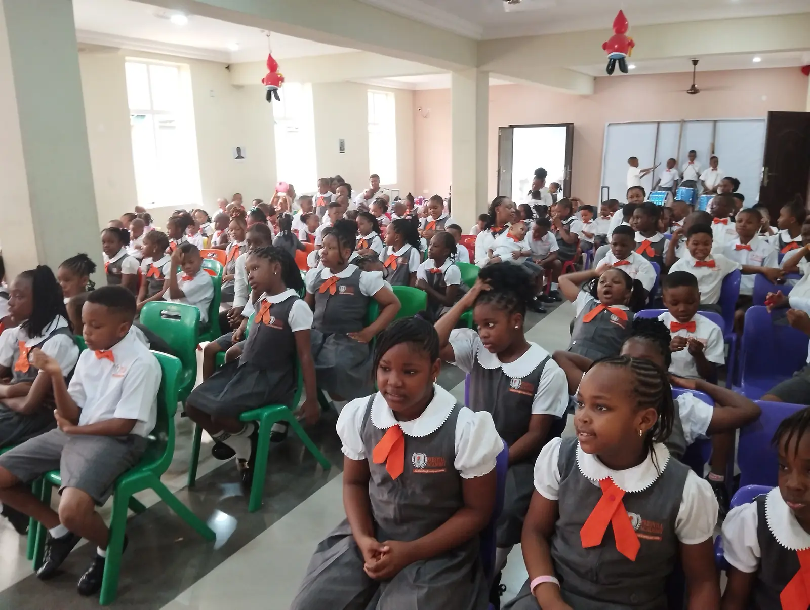 Pupils in uniform seated in rows of chairs in the school hall