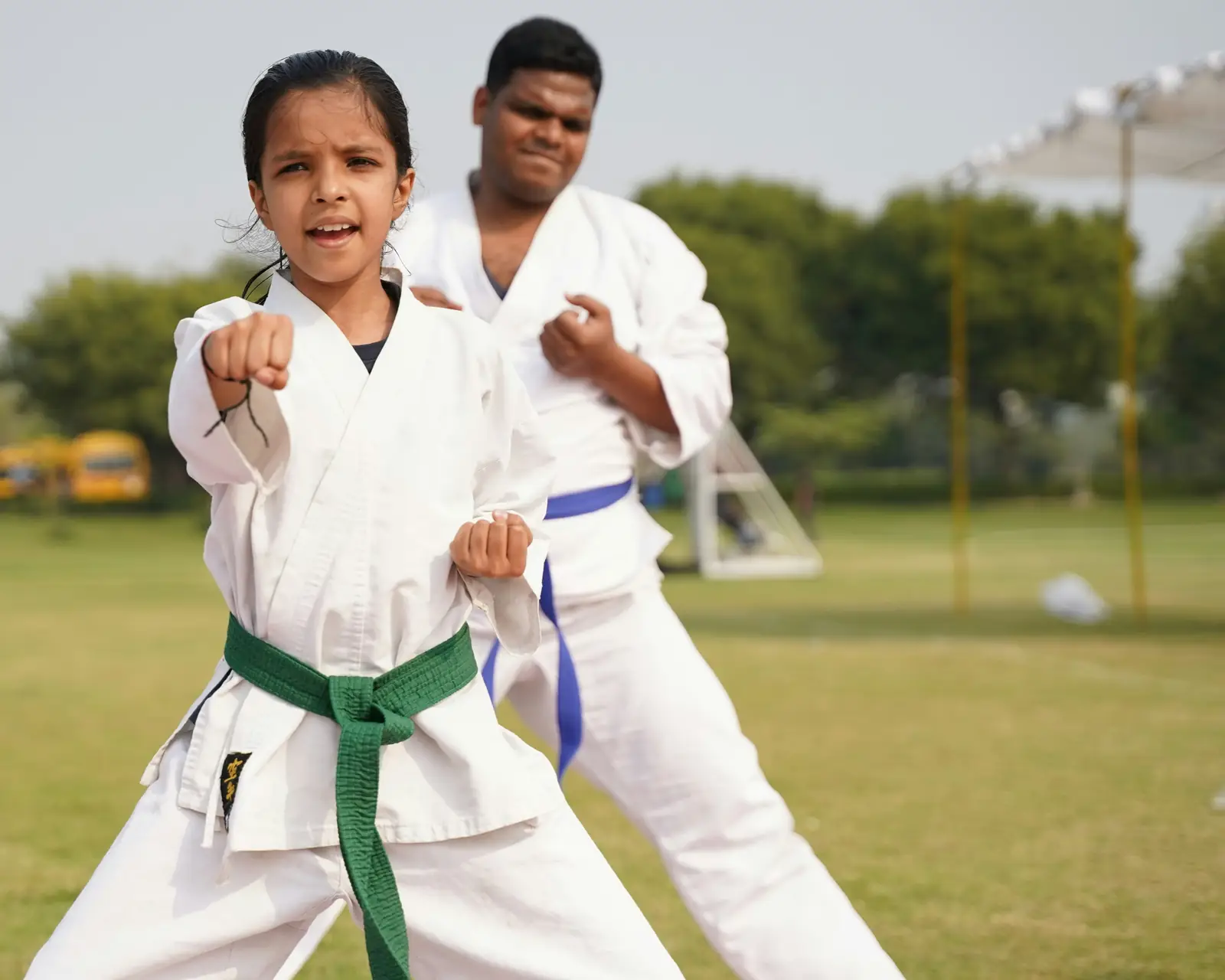 Illustrative photo: a girl in a white uniform and green belt practising a punch, with an instructor behind her