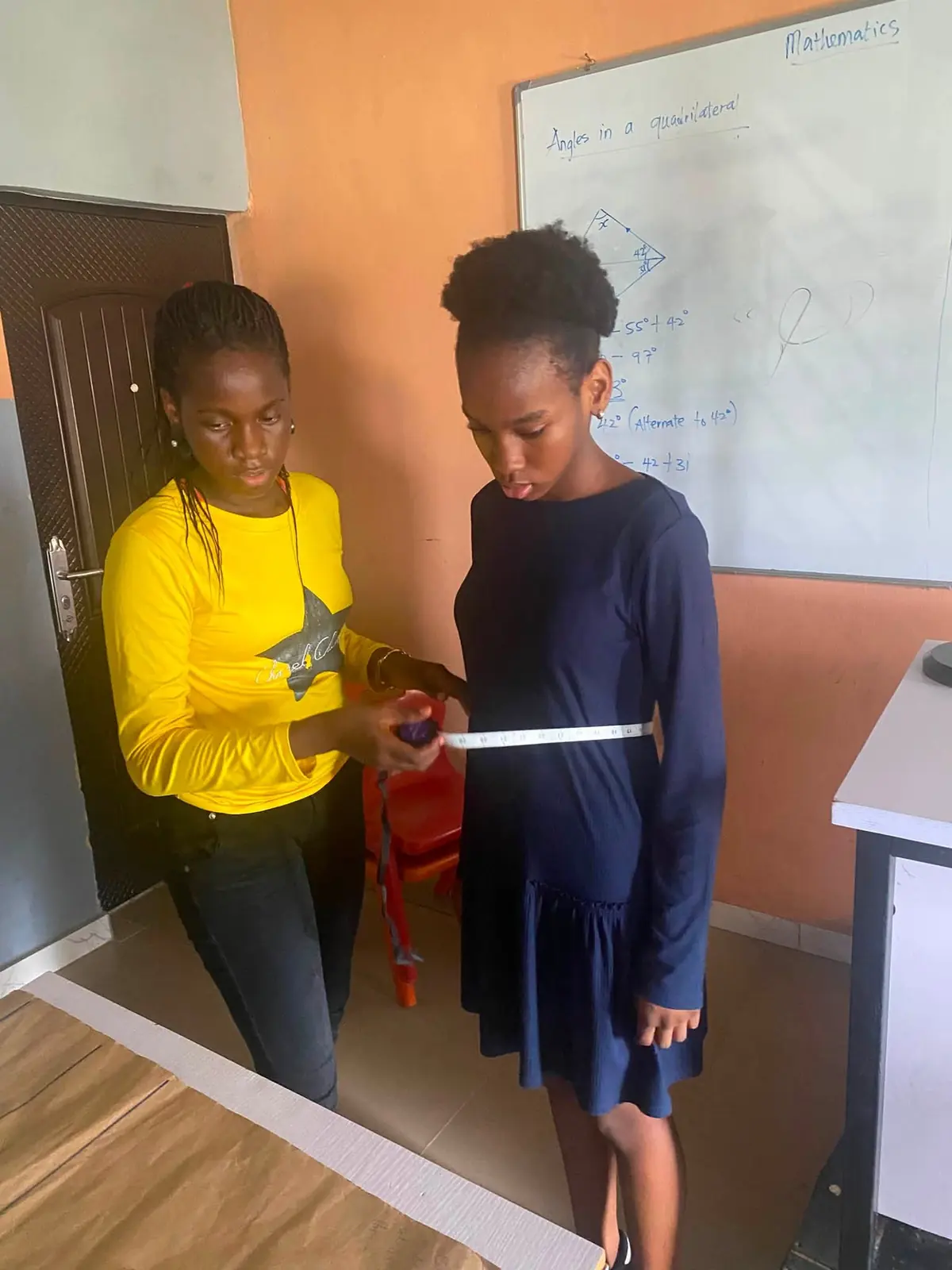 A pupil taking a classmate's waist measurement with a tape measure